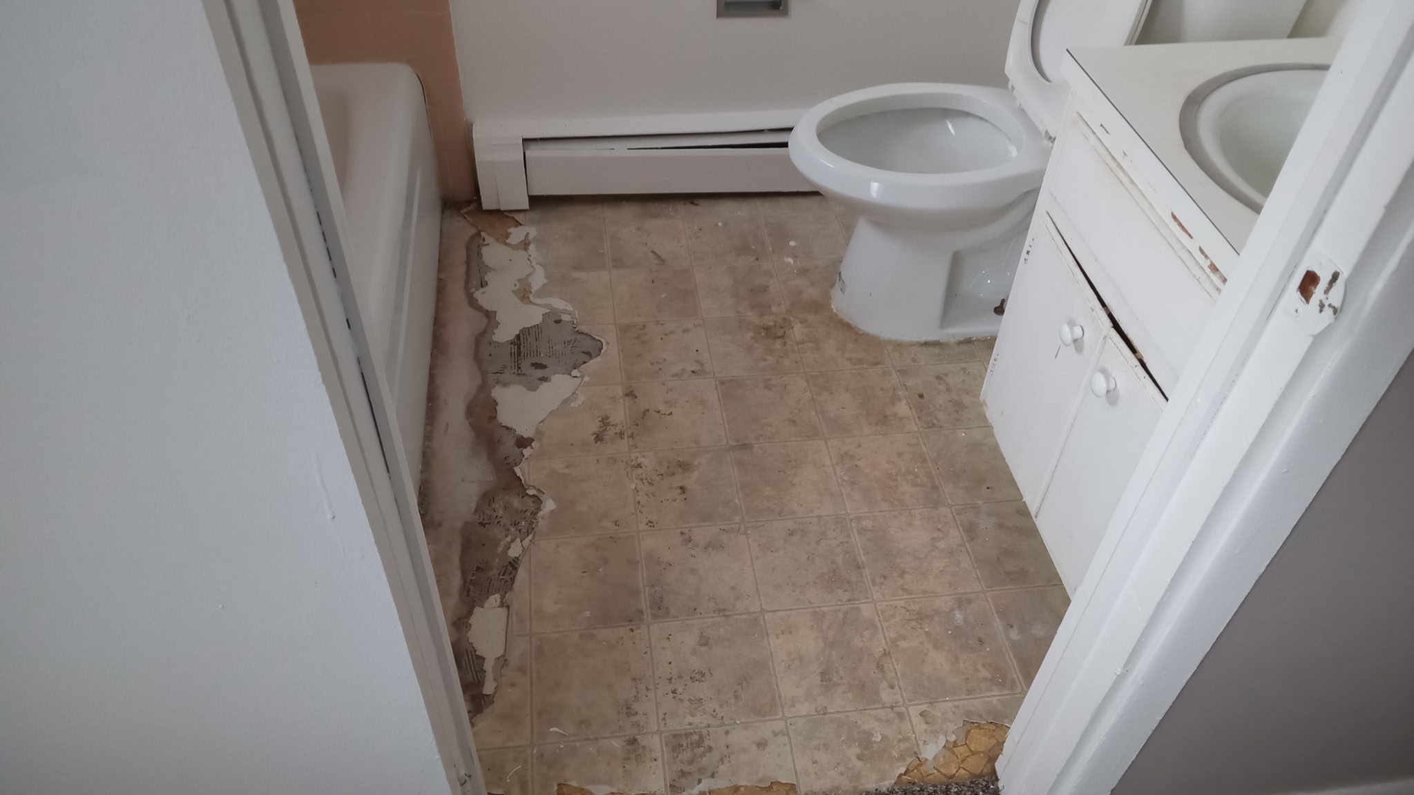 Bathroom before remodel — water-damaged, peeling vinyl tile floor