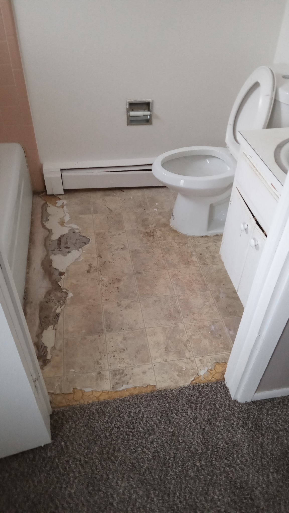 Bathroom before remodel — old worn tile and torn flooring at carpet edge
